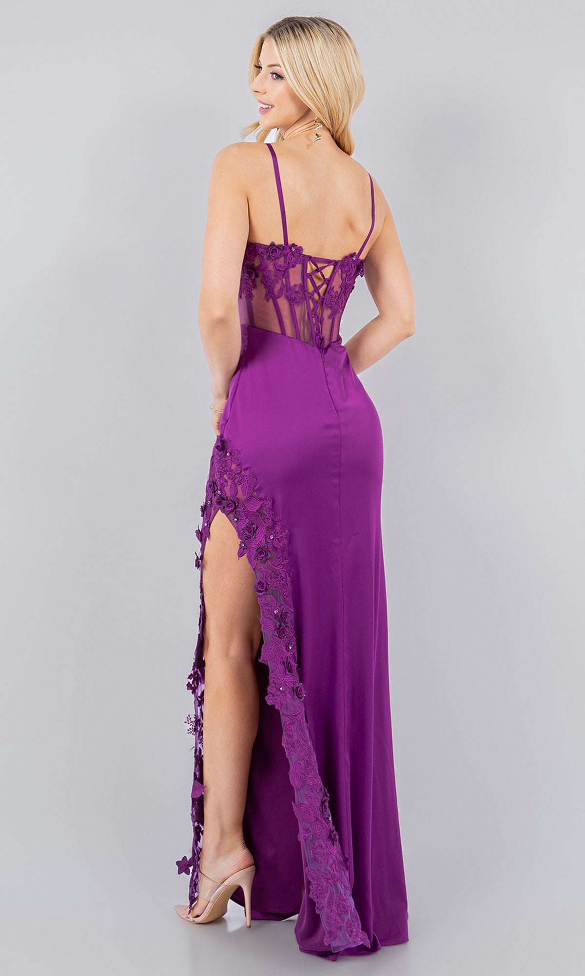 A woman wearing the Cinderella Couture 8085J long corset prom dress with floral lace, beaded embroidery, a high slit, and a sheer lace back stands gracefully, glancing over her shoulder in true fairy-tale style.
